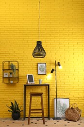 High wooden table with tablet and stool as stand up workplace near yellow brick wall. Stylish interior