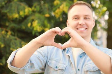 Man making heart with hands outdoors on sunny day, closeup