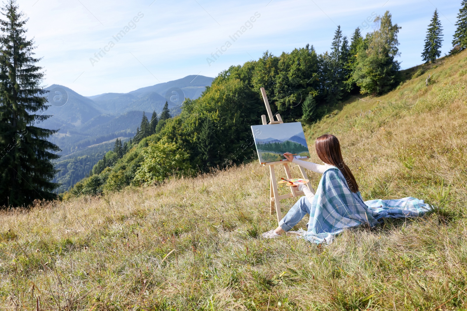 Photo of Young woman drawing on easel in mountains, back view. Space for text