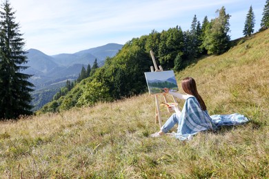 Photo of Young woman drawing on easel in mountains, back view. Space for text