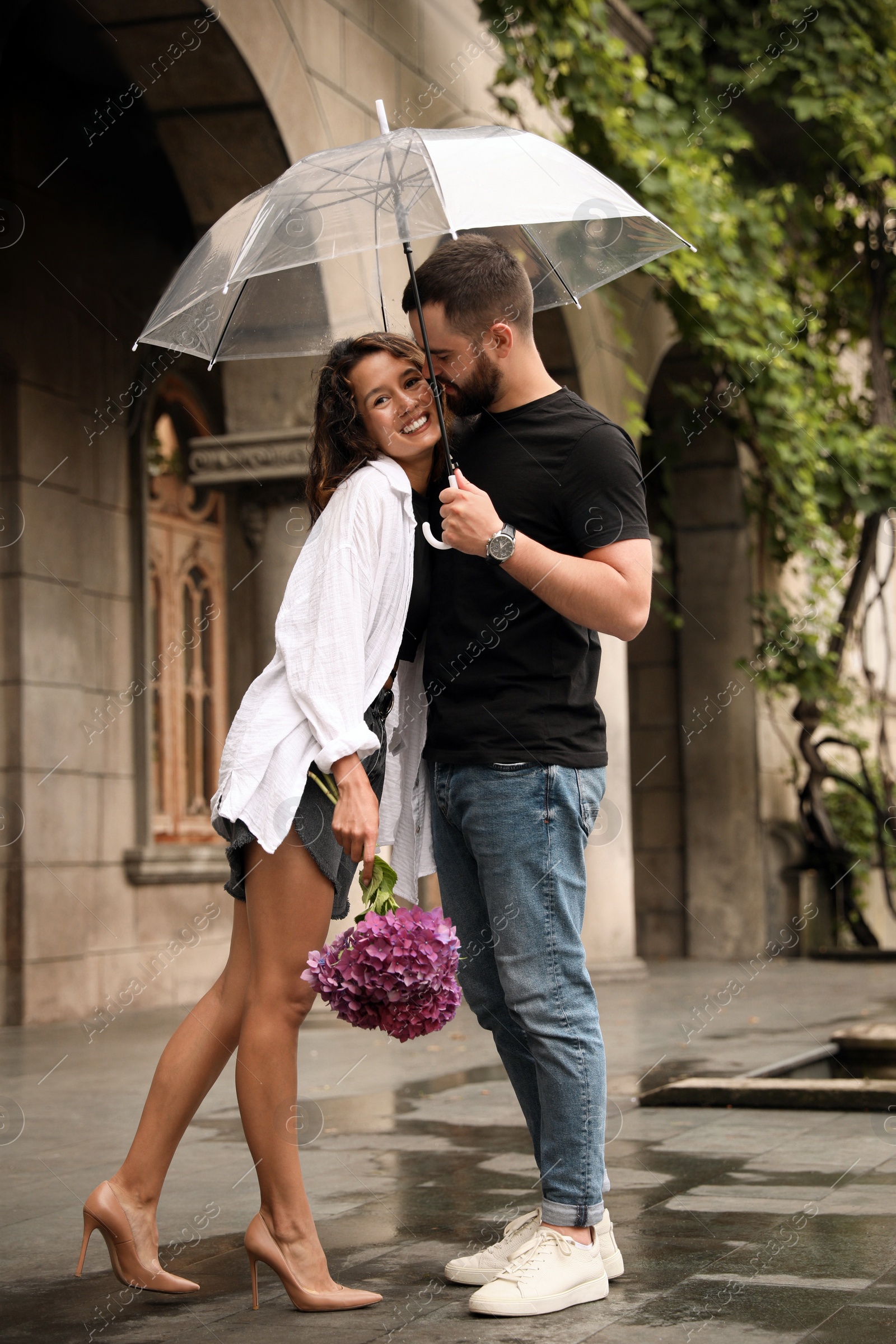 Photo of Young couple with umbrella enjoying time together under rain on city street