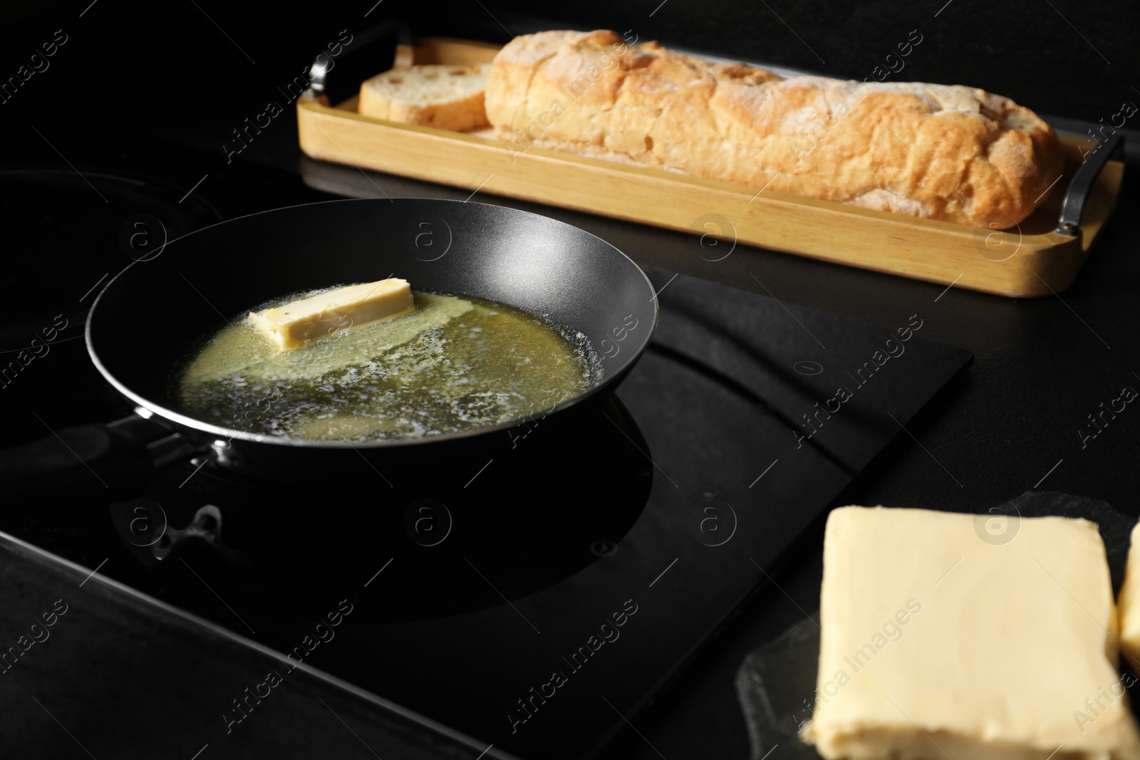 Photo of Melting butter in frying pan, dairy product and bread on black table