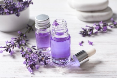 Glass bottles of natural cosmetic oil and lavender flowers on white wooden table