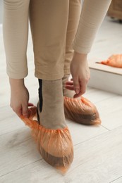 Photo of Woman wearing bright shoe covers onto her boots indoors, closeup