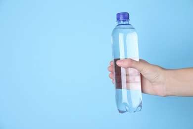 Photo of Woman holding plastic bottle with water on light blue background, closeup. Space for text