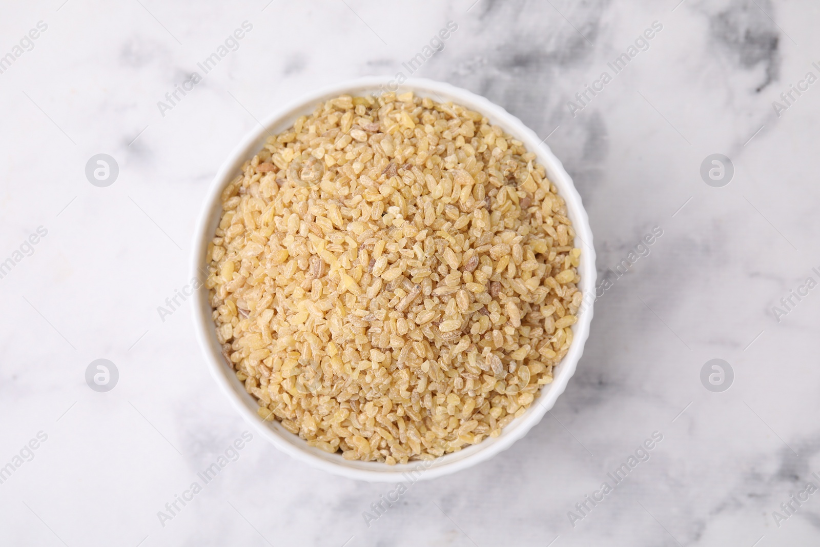 Photo of Raw bulgur in bowl on marble table, top view