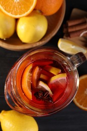 Glass jug of aromatic punch drink and ingredients on black wooden table, flat lay