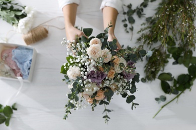 Photo of Florist holding beautiful wedding bouquet at white table, top view