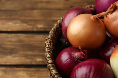 Onion bulbs in basket on wooden table, closeup