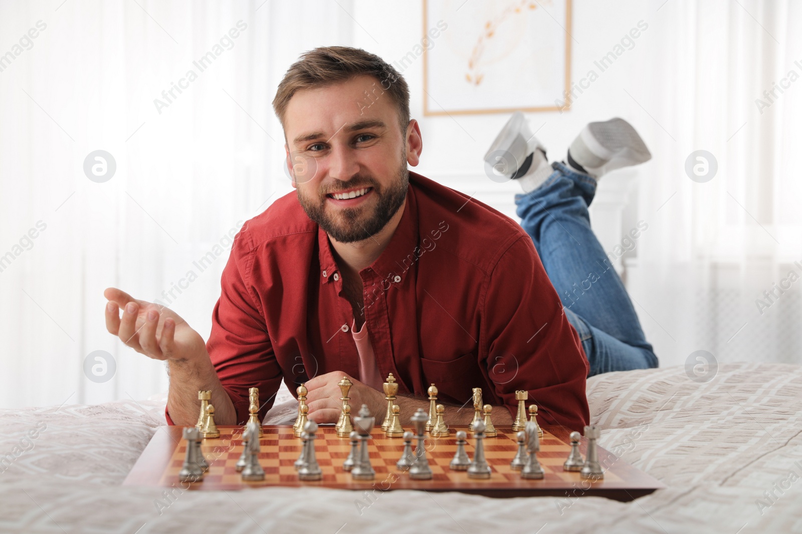 Photo of Happy young man playing chess on bed at home