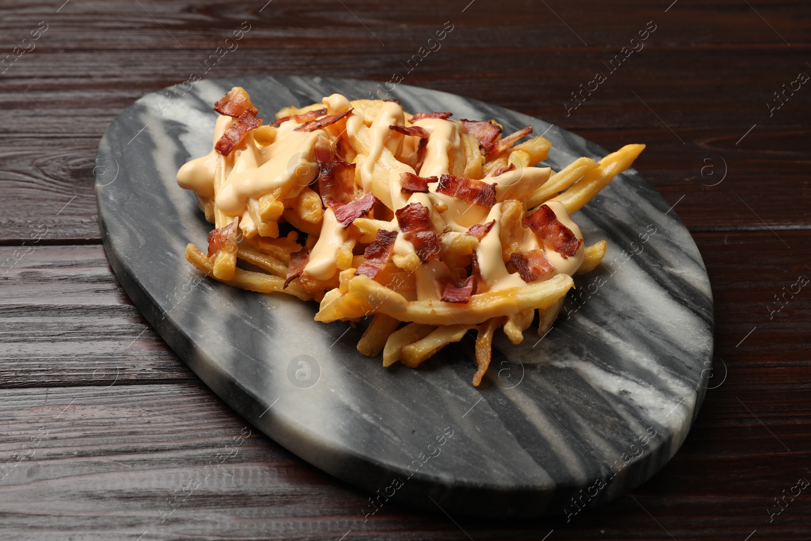 Photo of Delicious French fries with bacon and cheese sauce on wooden table, closeup