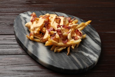 Photo of Delicious French fries with bacon and cheese sauce on wooden table, closeup