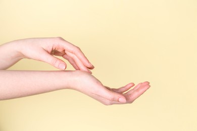 Woman applying cream on her hand against yellow background, closeup