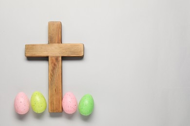 Wooden cross and painted Easter eggs on light grey background, flat lay. Space for text