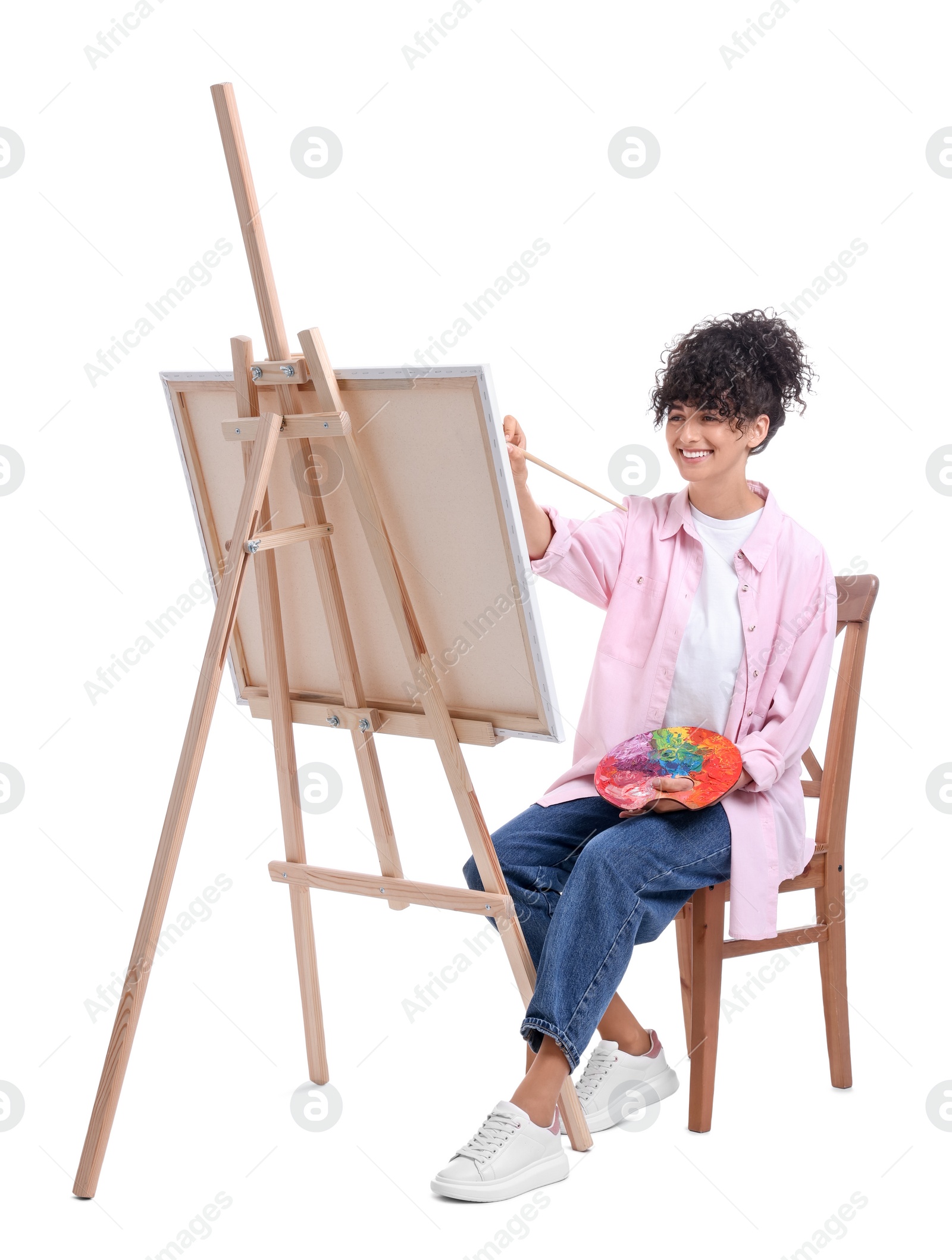 Photo of Young woman painting on easel with canvas against white background