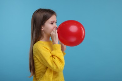 Cute girl inflating red balloon on light blue background
