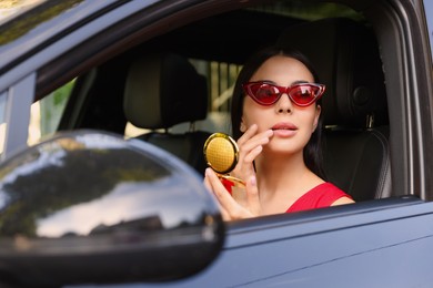 Beautiful young woman with cosmetic pocket mirror in car