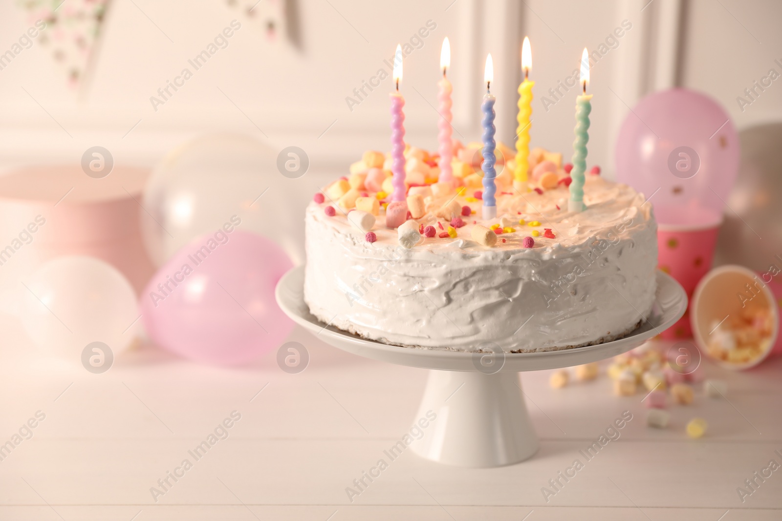 Photo of Tasty Birthday cake with burning candles and party decor on white table