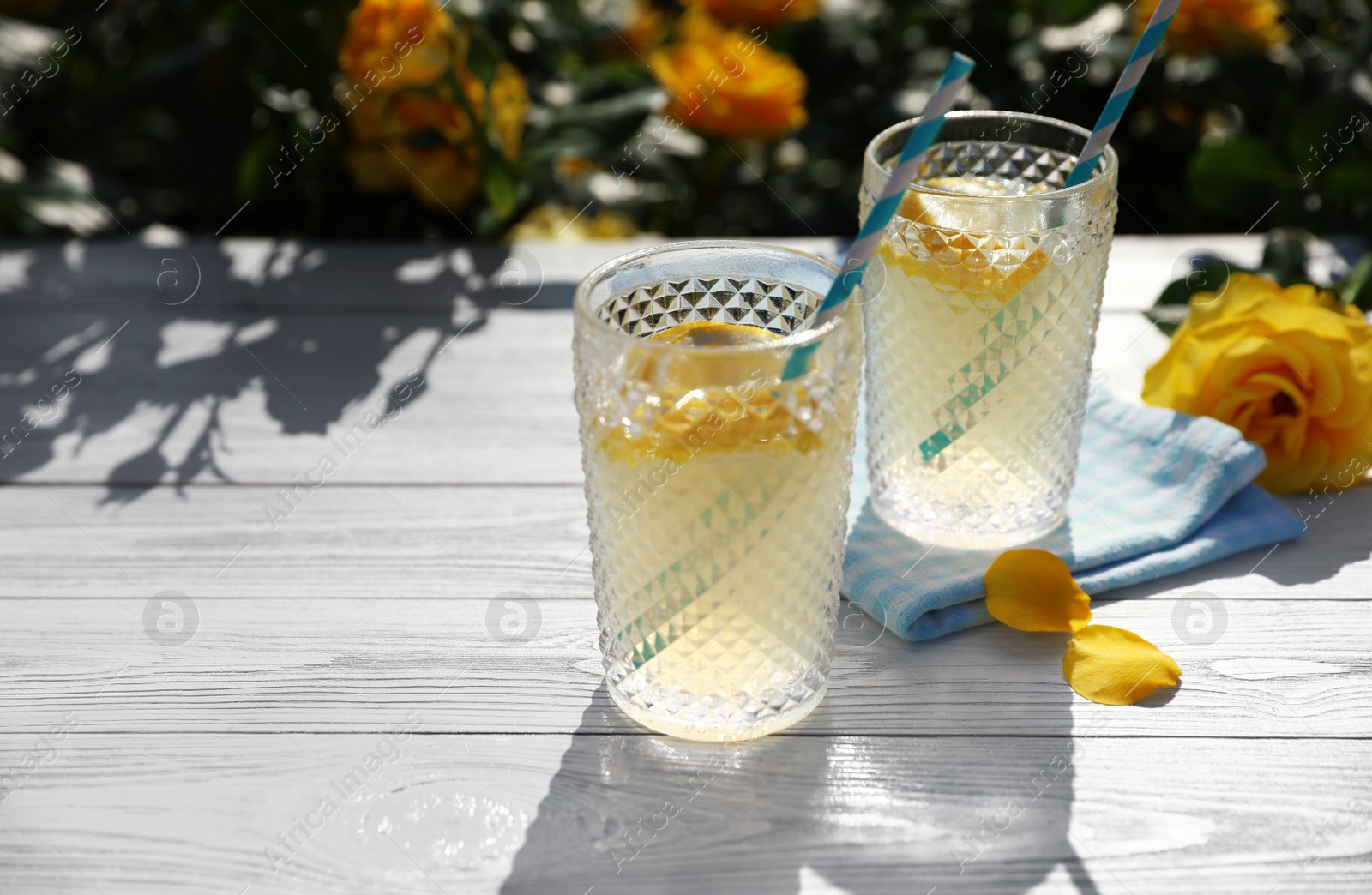 Photo of Glasses of refreshing lemonade on white wooden table in rose garden. Space for text