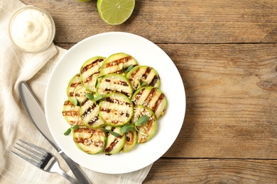 Photo of Delicious grilled zucchini slices served with sauce and lime on wooden table, flat lay. Space for text