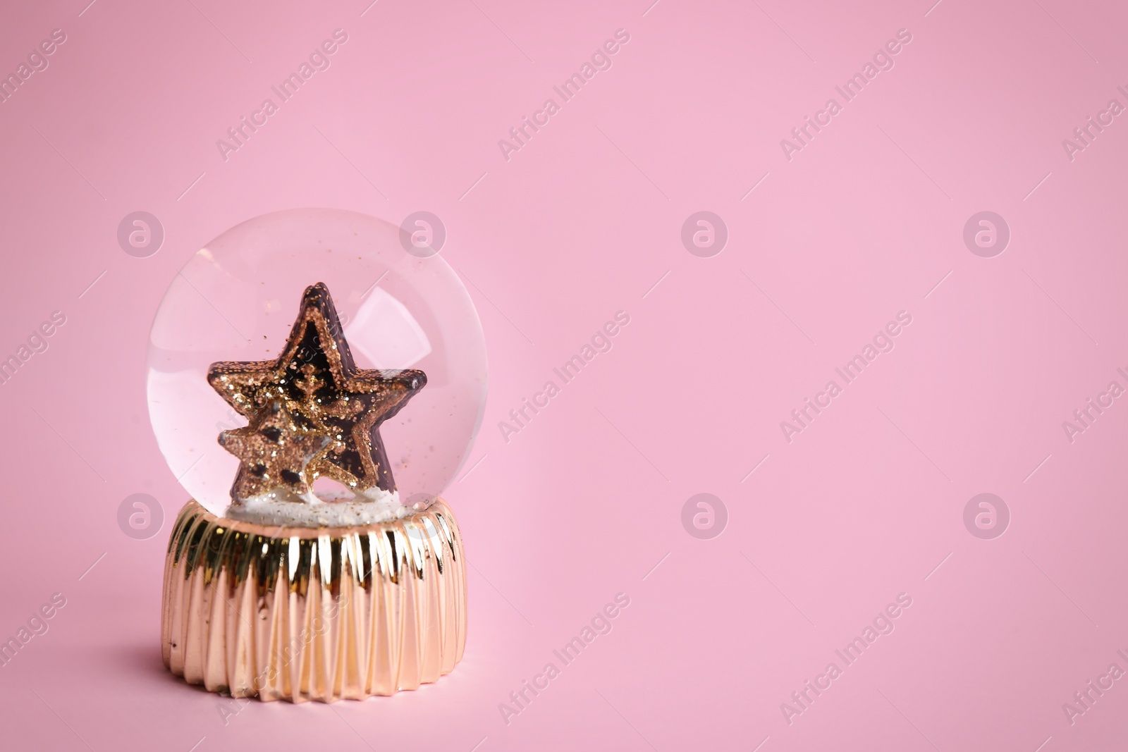 Photo of Beautiful snow globe with stars on pink background, space for text