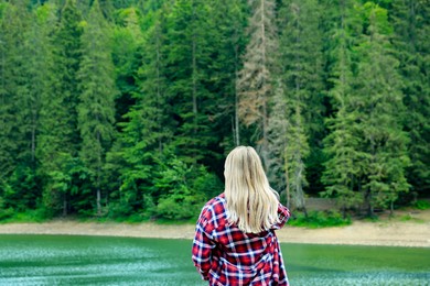 Woman near clear lake and green forest at summer, space for text