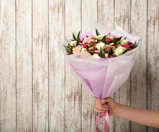 Woman holding beautiful bouquet of flowers and chocolate candies on white wooden background, closeup. Space for text