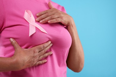 Woman with pink ribbon on light blue background, closeup and space for text. Breast cancer awareness
