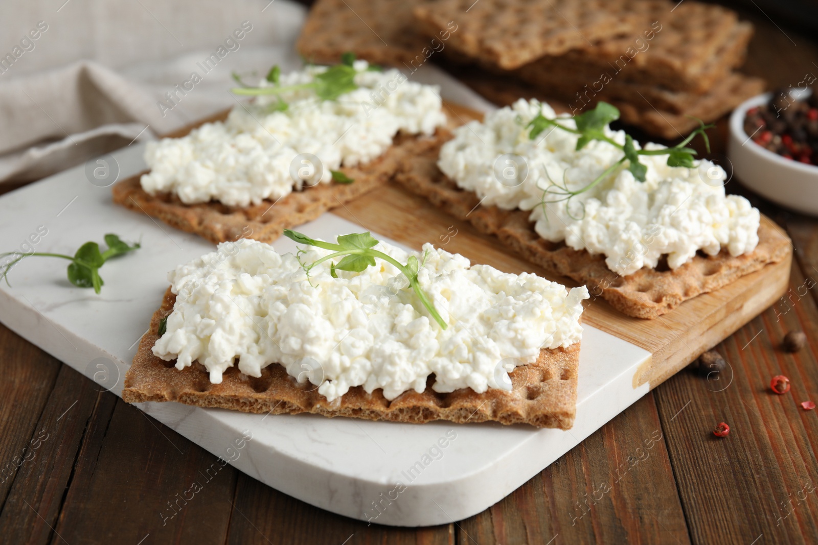 Photo of Crispy crackers with cottage cheese and microgreens on wooden table, closeup