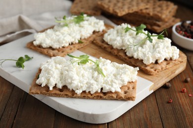 Photo of Crispy crackers with cottage cheese and microgreens on wooden table, closeup