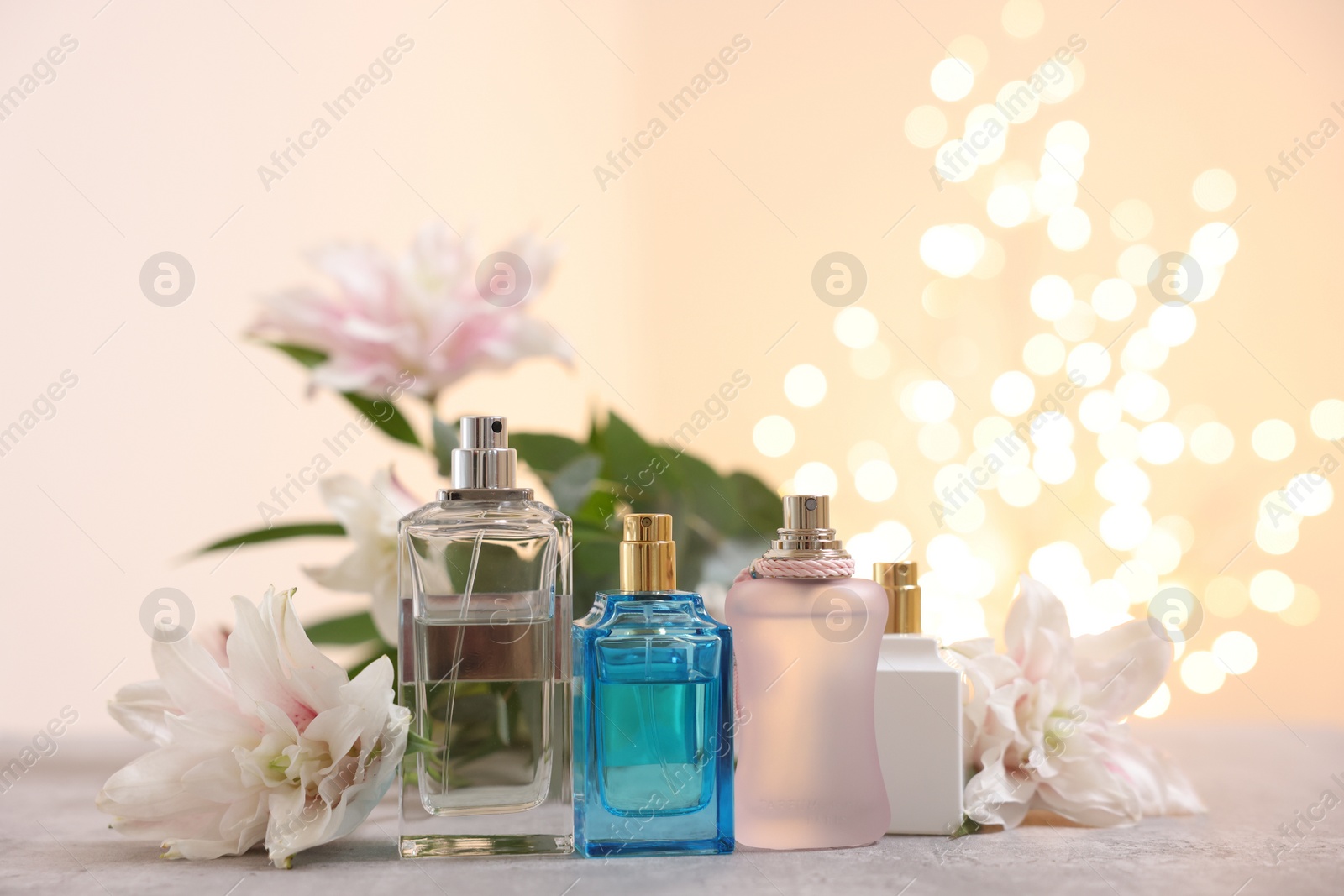 Photo of Perfume bottles and bouquet of beautiful lily flowers on table against beige background with blurred lights, closeup