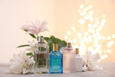 Photo of Perfume bottles and bouquet of beautiful lily flowers on table against beige background with blurred lights, closeup