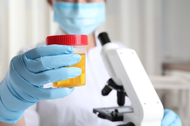 Photo of Doctor holding container with urine sample for analysis in laboratory, focus on hand
