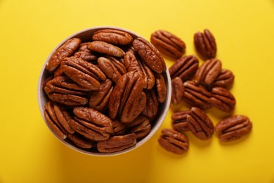 Photo of Tasty pecan nuts with bowl on yellow background, flat lay