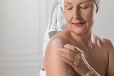 Happy woman applying body cream onto shoulder near white wall. Space for text