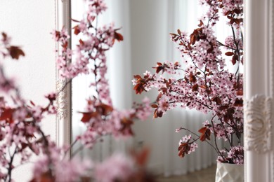 Photo of Blossoming tree twigs in vase near mirror indoors, closeup
