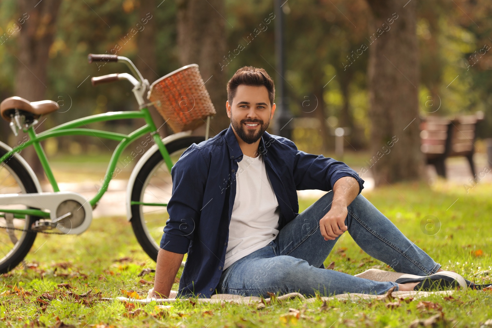 Photo of Young man sitting on green grass near bicycle in park