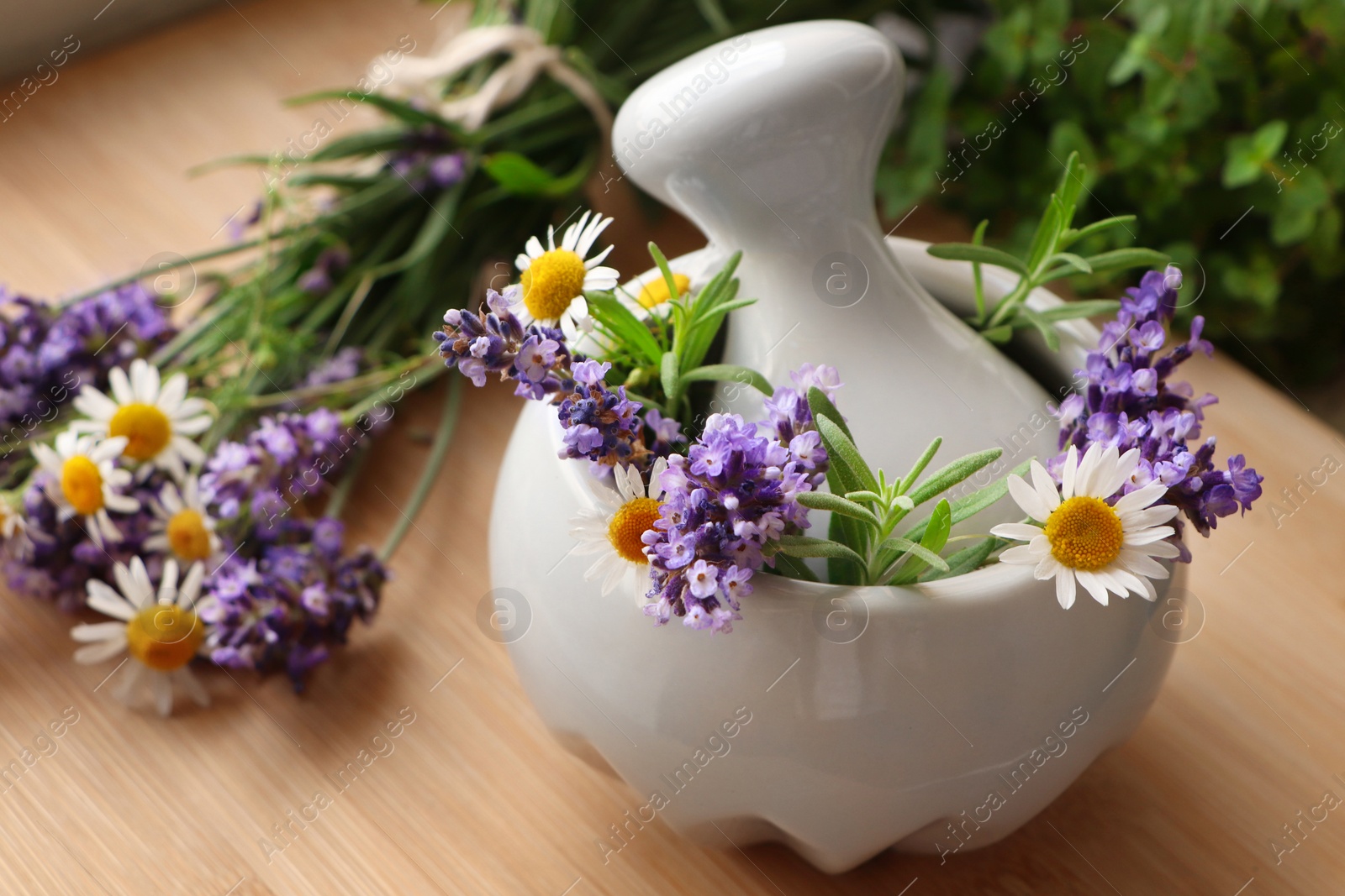 Photo of Mortar with fresh lavender, chamomile flowers, rosemary and pestle on wooden table