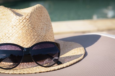 Photo of Stylish hat and sunglasses near outdoor swimming pool, closeup. Space for text