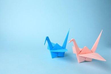 Photo of Origami art. Colorful handmade paper cranes on light blue background, space for text