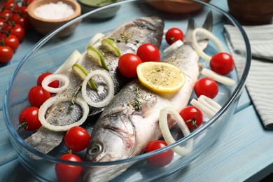 Glass baking tray with sea bass fish and ingredients on light blue wooden table, closeup