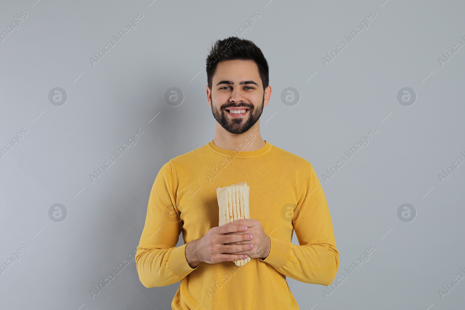 Photo of Happy young man holding tasty shawarma on grey background