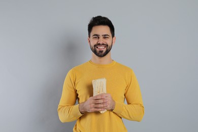 Happy young man holding tasty shawarma on grey background