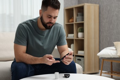 Photo of Diabetes test. Man checking blood sugar level with lancet pen at table indoors