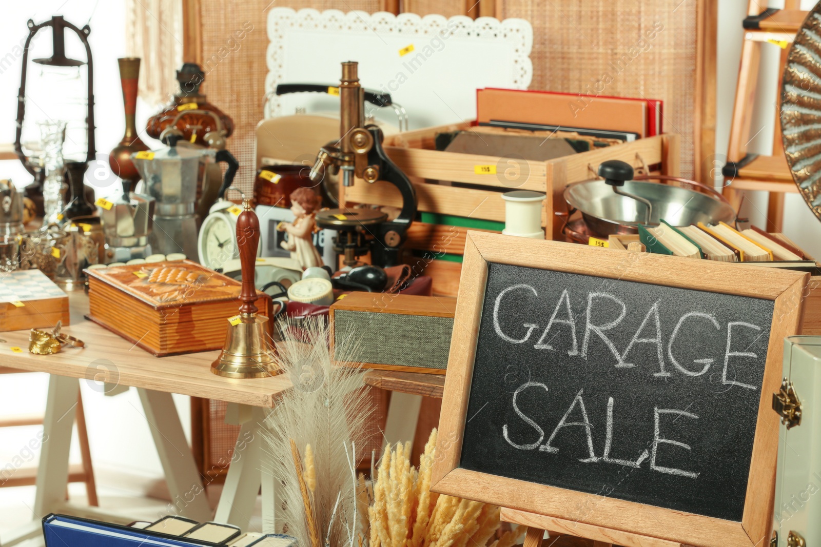 Photo of Sign Garage Sale written on blackboard near many different stuff indoors