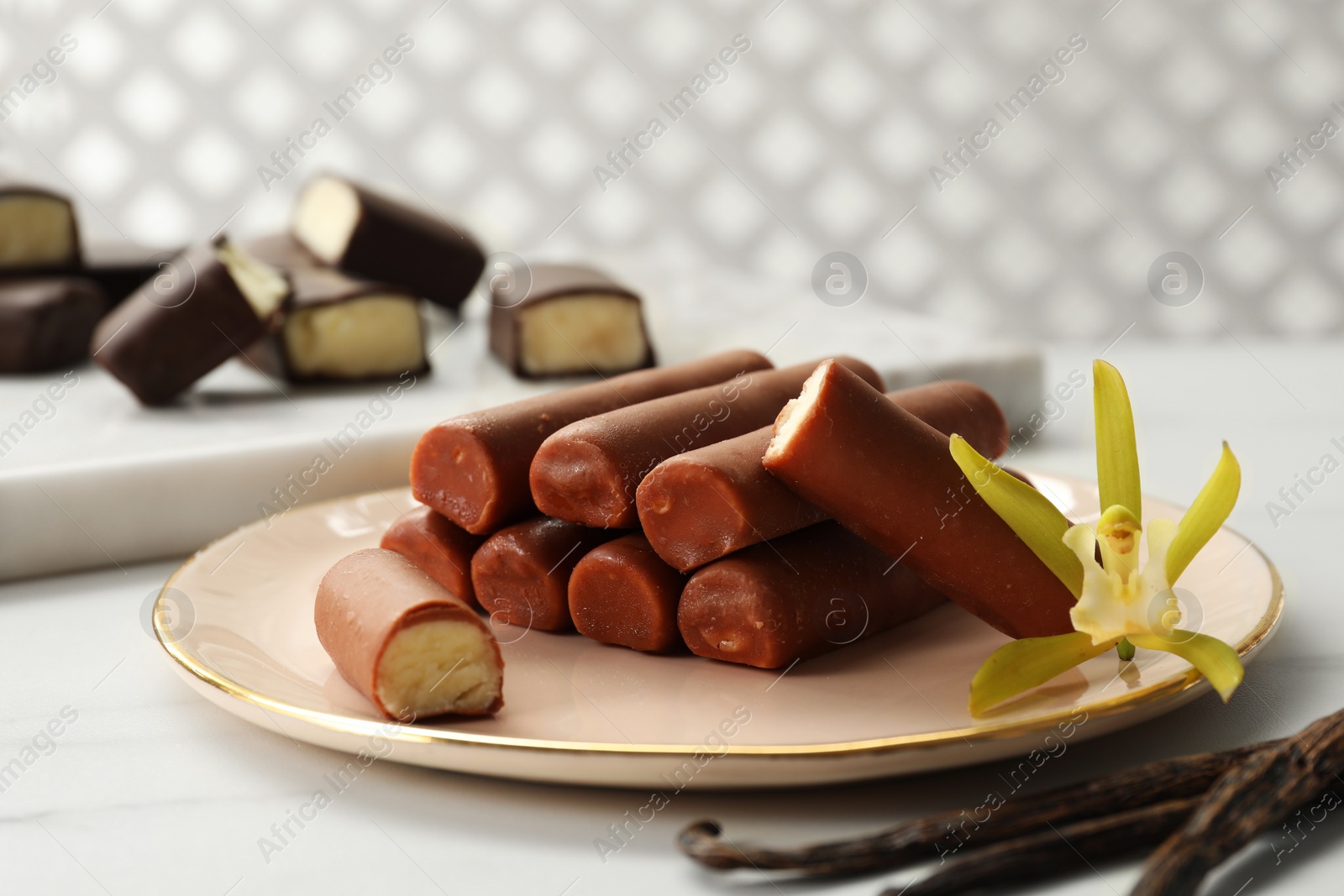 Photo of Glazed curd cheese bars, vanilla pods and flower on white marble table, closeup