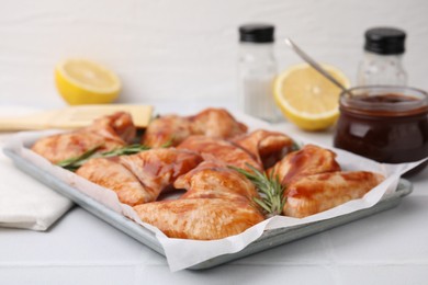 Photo of Raw marinated chicken wings and rosemary on light tiled table, closeup