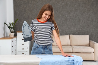 Young woman ironing clothes on board at home