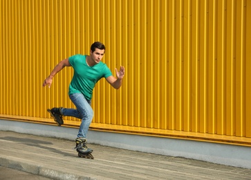 Handsome young man roller skating near yellow building, space for text