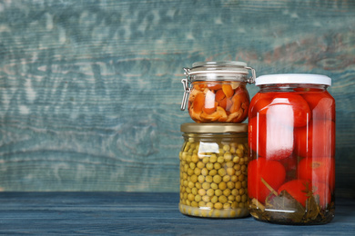 Photo of Glass jars with different pickled vegetables on blue wooden table. Space for text